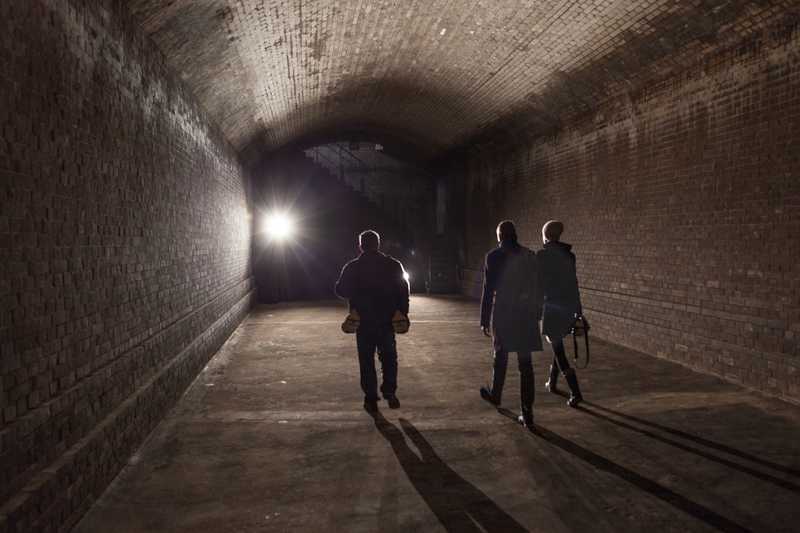 Drei Menschen laufen im Dunkel des Berliner Wasserspeichers dem Licht entgegen
